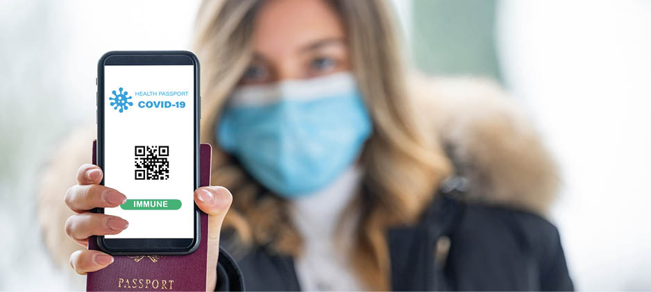 (Selective focus, focus on the smart phone) A defocused young girl, wearing a face mask, is holding a passport and a smart phone with a digital illustration of a Covid-19 Health Passport concept 