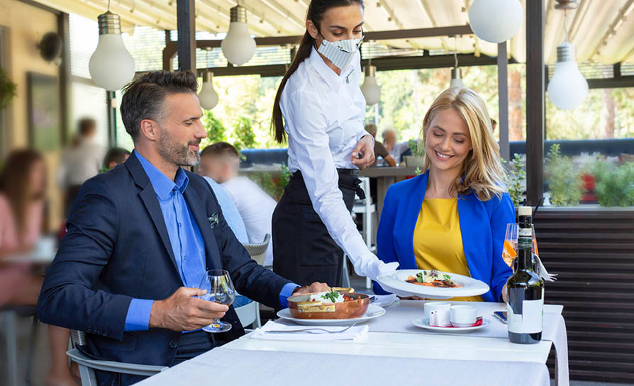 Handsome couple having lunch in the restaurant, being served by waitress with a mask, corona time