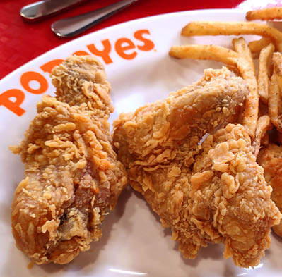 Saigon Vietnam: 1 May 19: Delicious spicy deep fried chicken wing nibbles Popeyes on white plate french fried potato chips unhealthy fast food snack dinner Western cuisine 