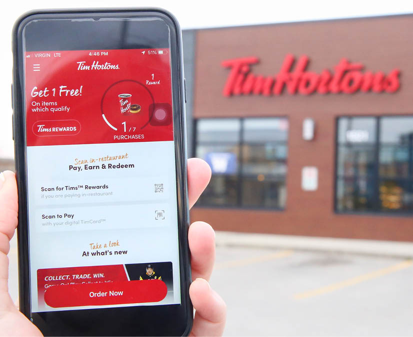 Winnipeg; Manitoba   Canada - October 8; 2019: Close-up of the Tim Hortons App with a Tim Hortons Store in the Background 