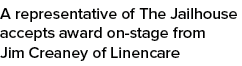 A representative of The Jailhouse accepts award on stage from Jim Creaney of Linencare