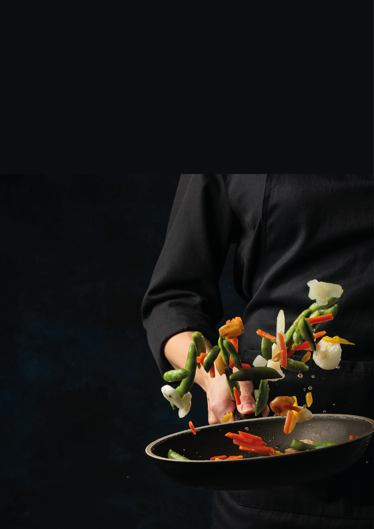 Chef in black uniform throws up colored vegetables above the pan on dark blue background. Backstage of cooking meal. Frozen motion. Food banner concept. Cookbook illustration.