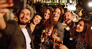 Selfie time. Group of friends at a nightclub party taking selfie with the phone. Young people enjoying having drinks together at the bar and make a photo of themselves on a phone. Winter holidays.