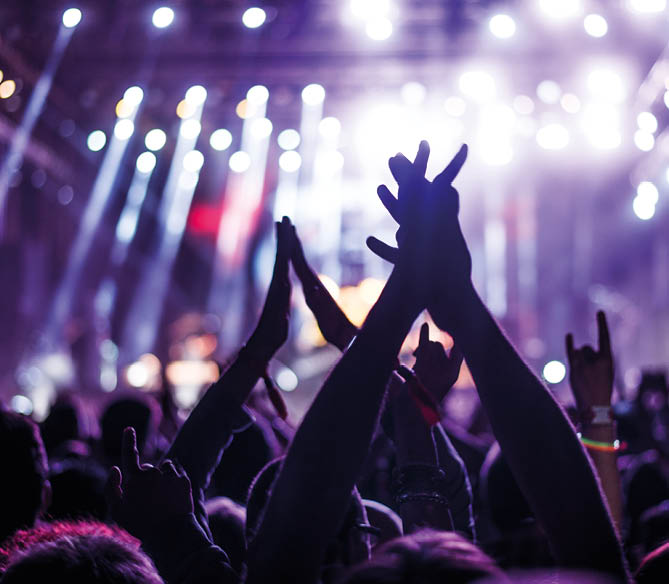 Audience with hands raised at a music festival and lights streaming down from above the stage  Soft focus, blurred movement 