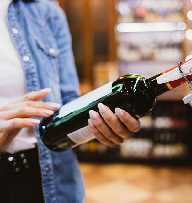 Close-up female hands holding bottle of wine in supermarket 