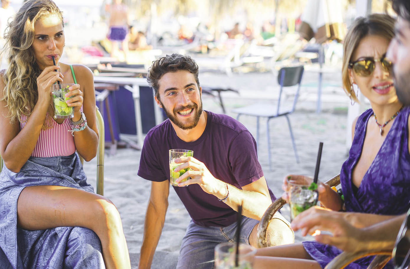 Group of happy young people hangout at the beach bar drinking long drinks cocktails together  Togetherness and friendship concept of friends gathering in the summertime 