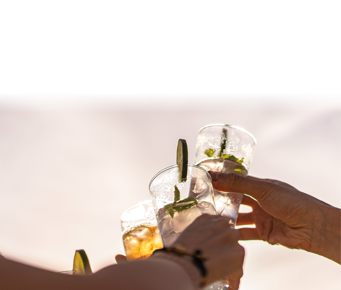 Friends rising cocktail glasses for a celebratory toast against the sky in the summer