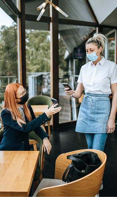 Young attractive business woman sitting in a restaurant or cafe bar and showing digital Covid-19 immunization pass certificate to the waitress  Pandemic and global security measures concept 