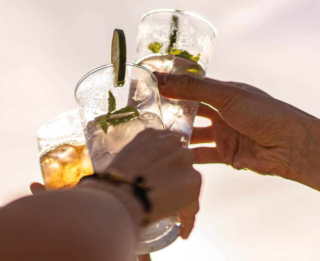 Friends rising cocktail glasses for a celebratory toast against the sky in the summer