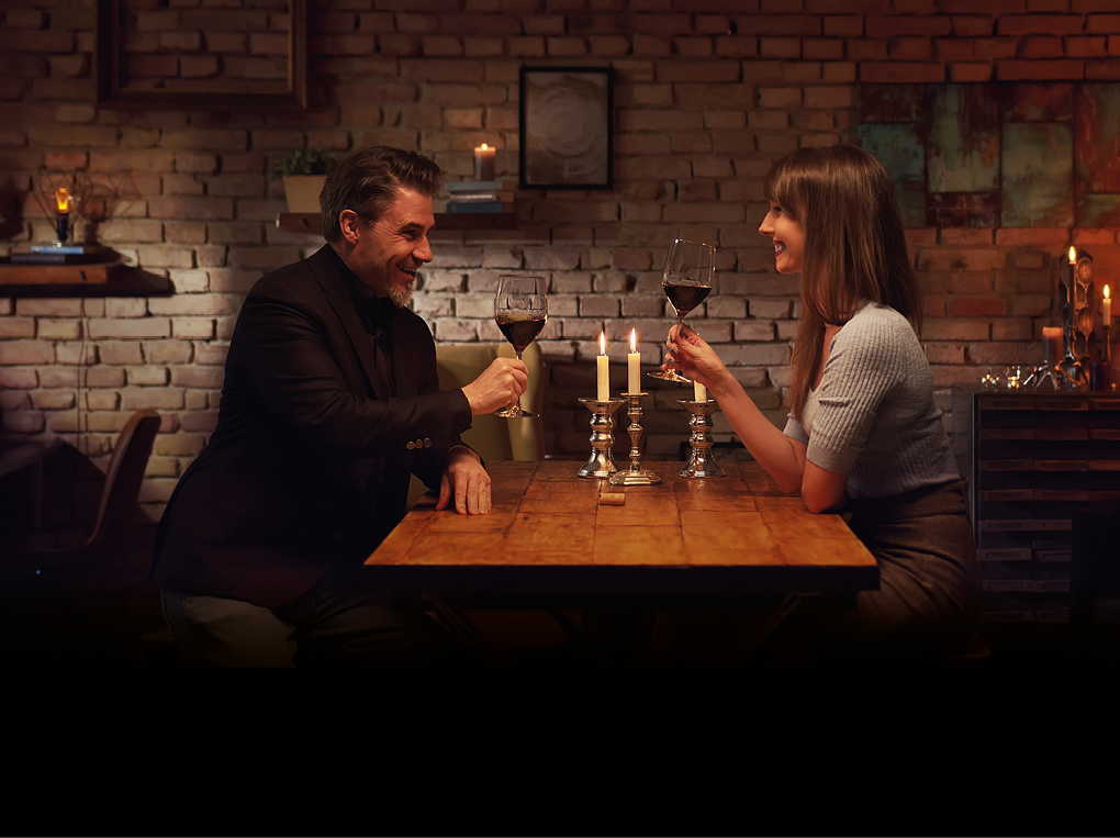 Elegant couple having romantic dinner at home, sitting at table in living room drinking red wine, talking. Stay at home concept.