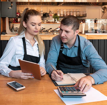 New small business owners counting revenue and expenses - Start-up entrepreneurs, woman and man, businessmen doing accounting with calculator and tablet in Restaurant