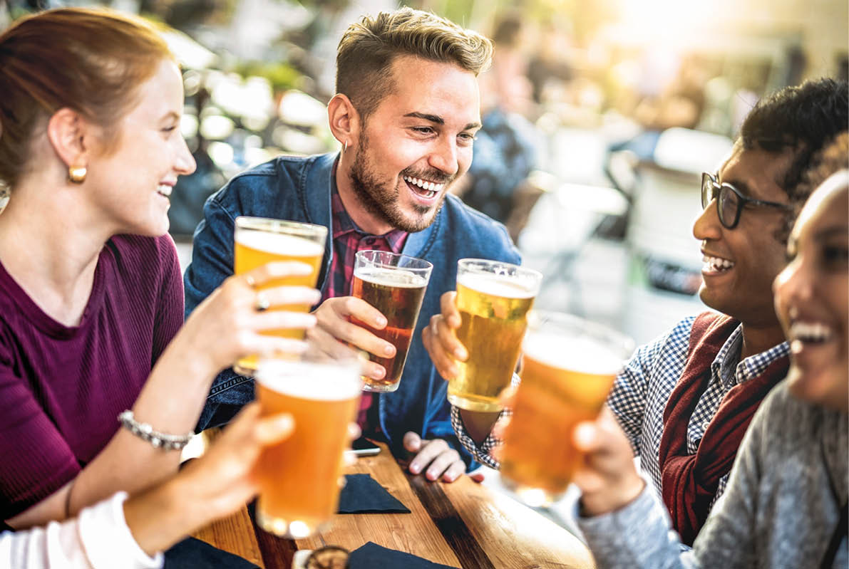 Young people drinking beer pints at brewery bar garden - Genuine beverage life style concept with guys and girls sharing happy hour together at open air pub dehor - Warm sunset backlight filter