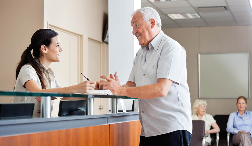 Senior man communicating with female receptionist while women sitting in background