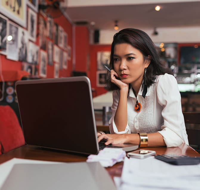 Pensive Asian bar owner using laptop to pay bills online