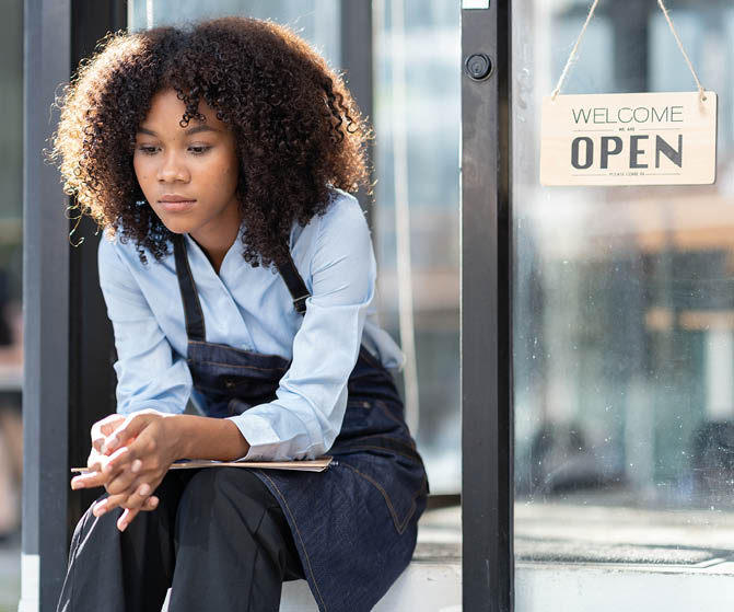 African barista woman in a barista uniform holding file showing stress and frustration sitting the entrance of a coffee shop there are no customers at the store