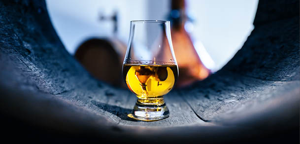 A glass of whiskey in old oak barrel. Copper alambic on background. Traditional alcohol distillery concept