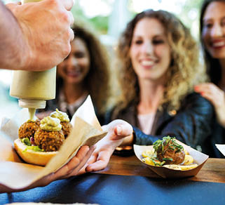 Portrait of three beautiful young women buying meatballs on a food truck in the park 