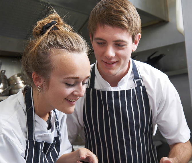 Chef Instructing Trainee In Restaurant Kitchen