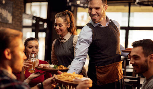 Happy waiters bringing food at the table and serving group of friends in a restaurant.