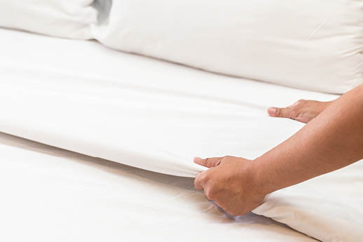Close up hand set up white bed sheet in hotel room