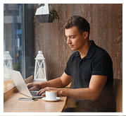 Handsome man working in cafe at window with coffee and laptop