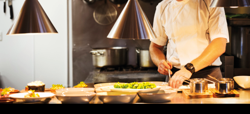 Chef standing in a restaurant kitchen, plating food.