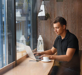 Handsome man working in cafe at window with coffee and laptop