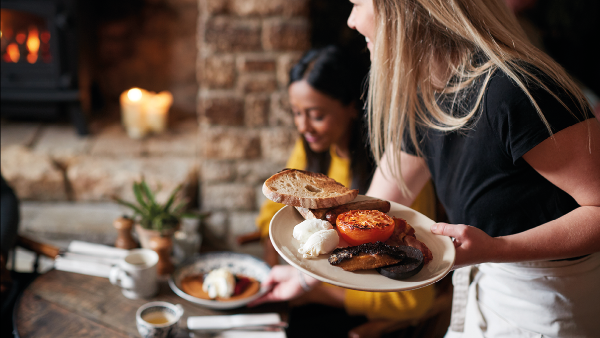 Close Up Of Waitress Working In Traditional English Pub Serving Breakfast To Guests