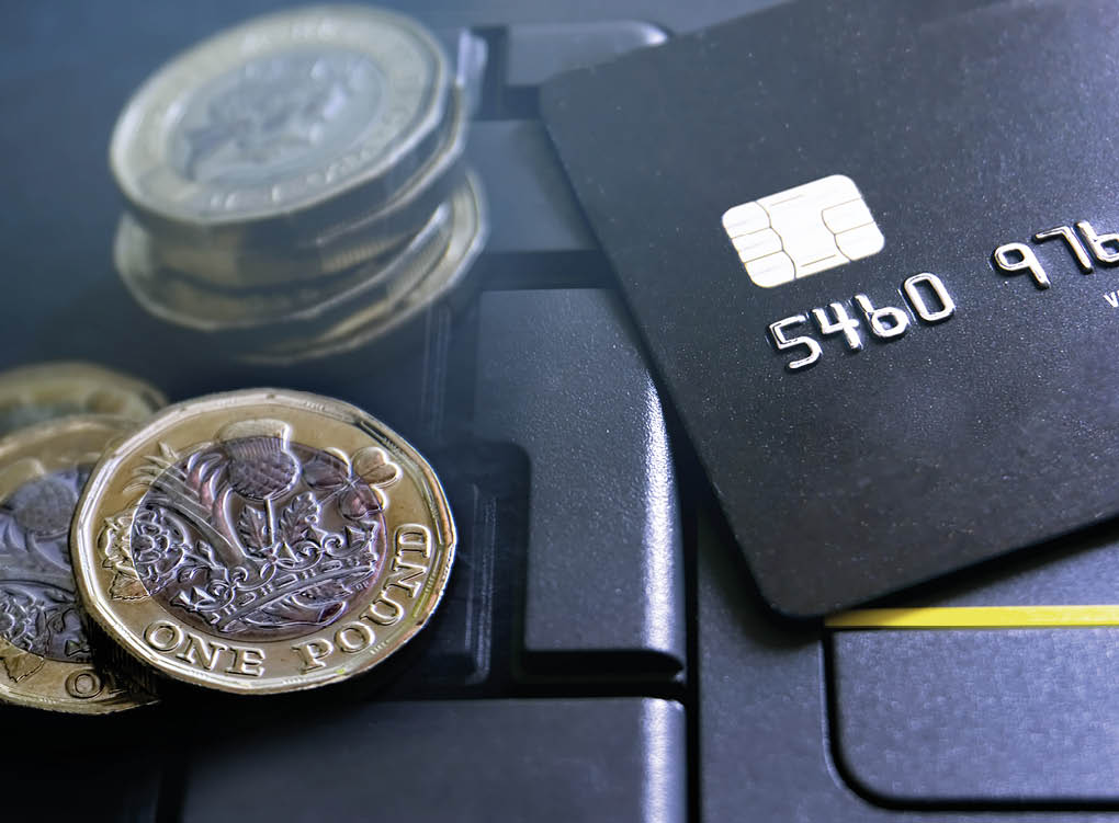 Double exposure of credit/debit cards on a laptop keyboard with new pound coins. Finance/money concept.
