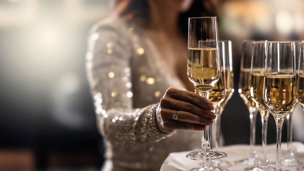 A bartender holds a plate with pink champagne and a woman in a cocktail dress takes one of the glasses at an event, party or wedding.
