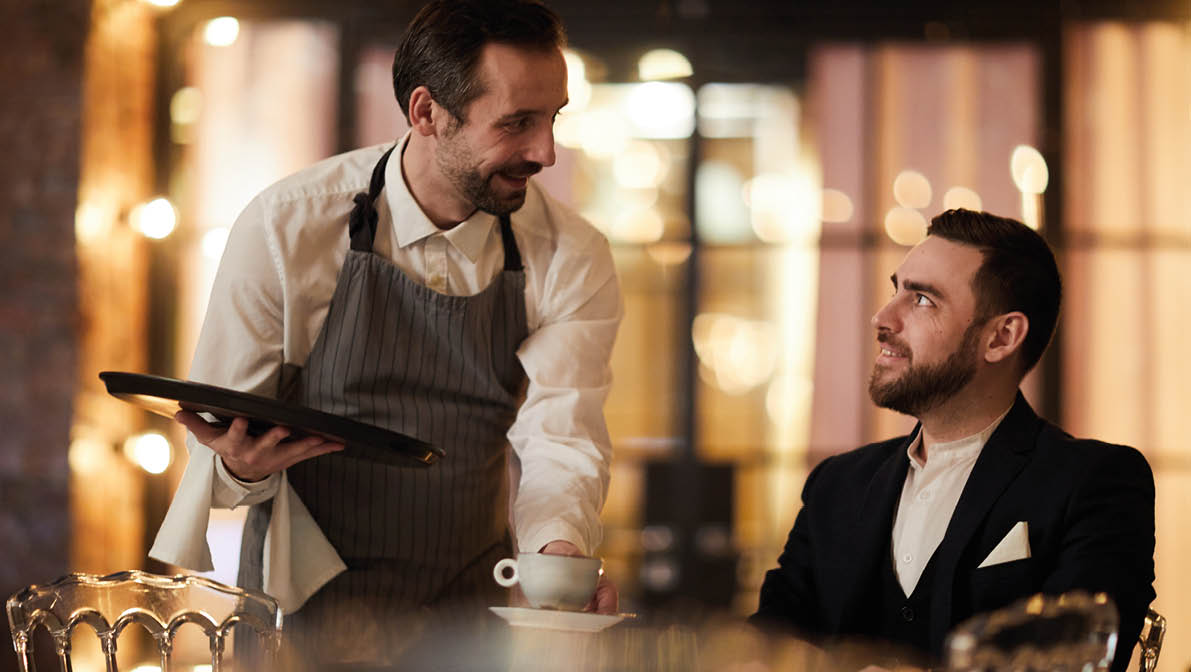 Portrait of mature waiter bringing coffee to client in luxury restaurant, copy space