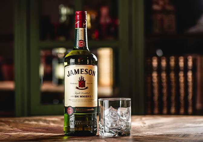 MOSCOW/RUSSIA - APRIL 24, 2018: Jameson whiskey bottle and glass with ice cubes on wooden table in dark bar. Jameson is a brand of traditional Irish whiskey from Dublin