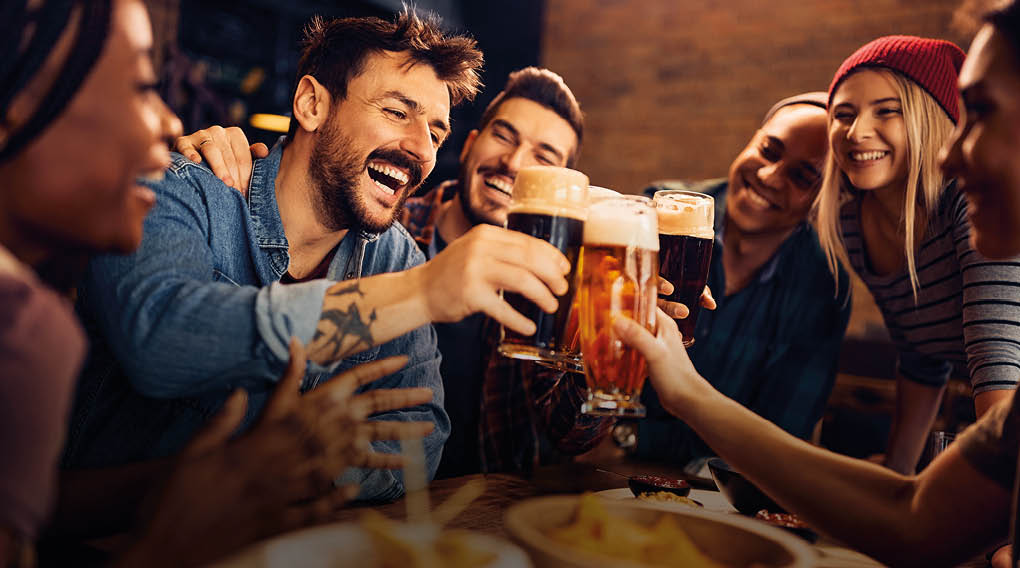 Multiracial group of happy friends having fun while toasting with beer in a bar.