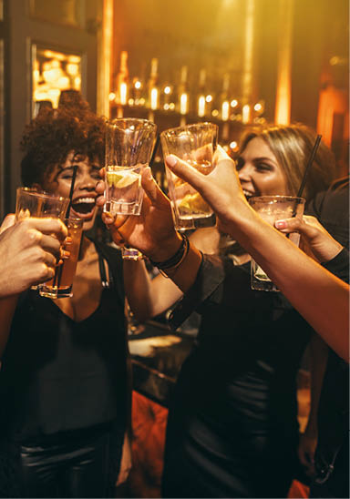 Group of men and women enjoying drinks at nightclub. Young people at bar toasting cocktails and laughing.