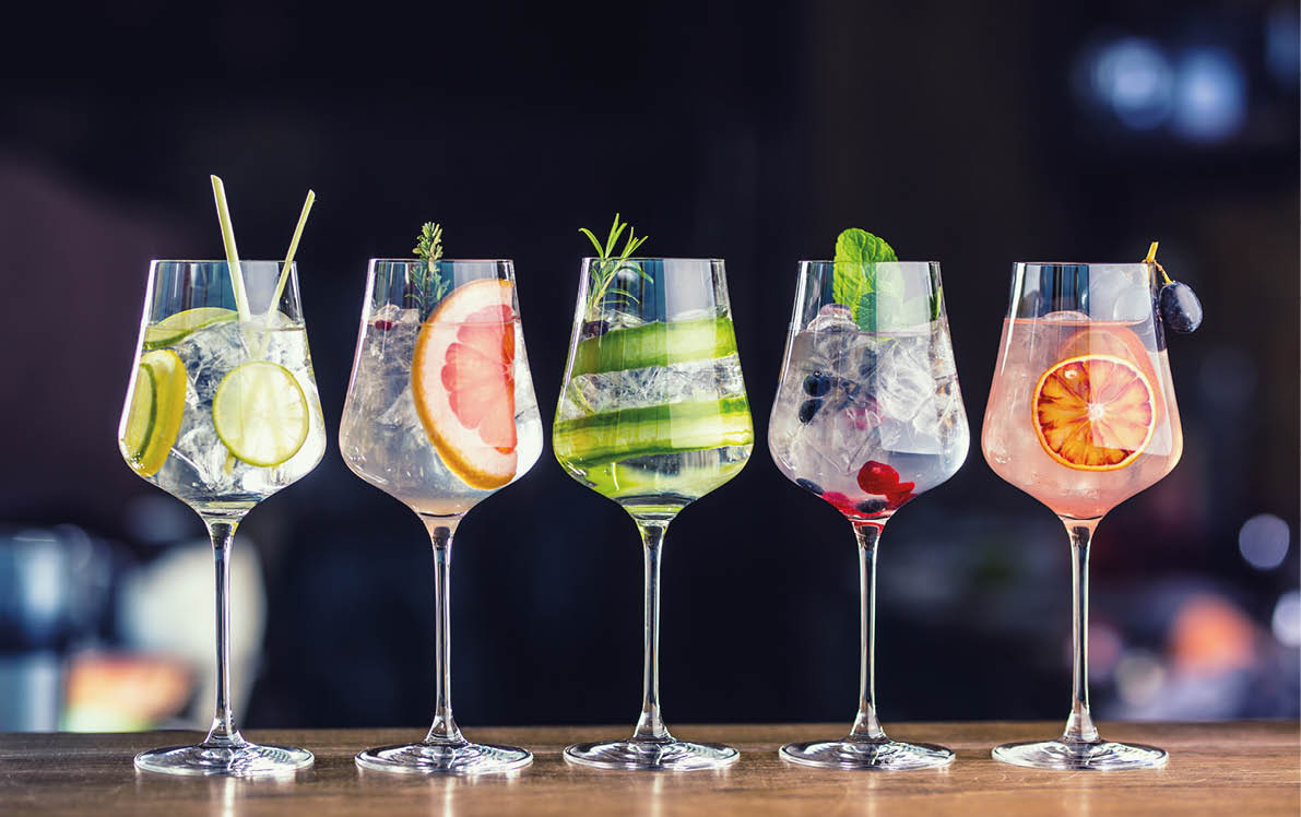 Five colorful gin tonic cocktails in wine glasses on bar counter in pup or restaurant. 