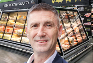 A man wearing a suit and tie standing in front of a meat and poultry display. Description generated by AI