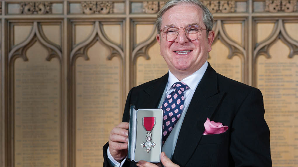 A man wearing a suit and tie is holding a medal. Description generated by AI