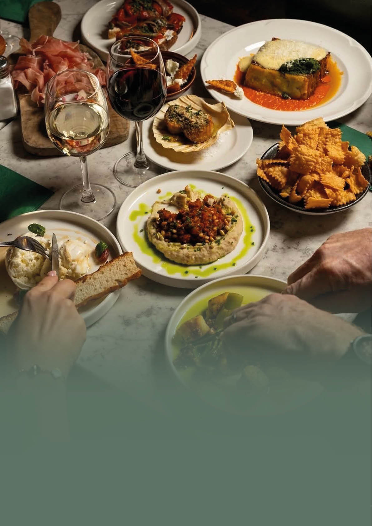 A table with plates of food and wine glasses. Description generated by AI