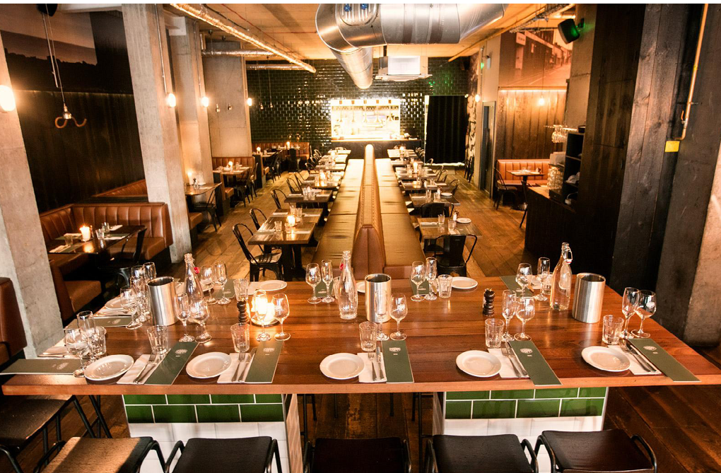 A restaurant with a long table set for dinner. Description generated by AI