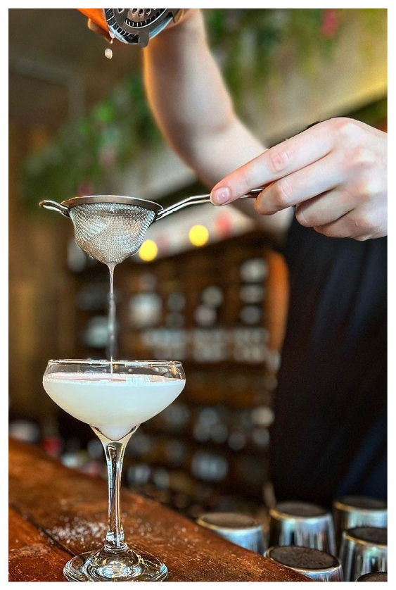 A glass of white liquid is being poured into a glass on a wooden bar. Description generated by AI