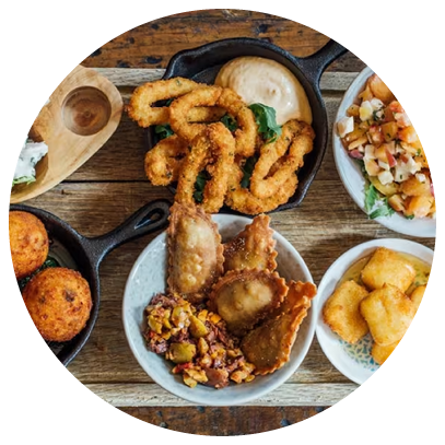 A wooden tray with a variety of foods including fried chicken, bread, and vegetables. Description generated by AI