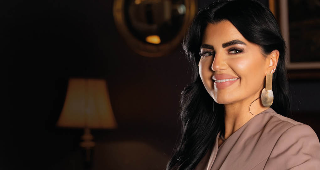 A woman wearing a brown jacket and earrings. Description generated by AI
