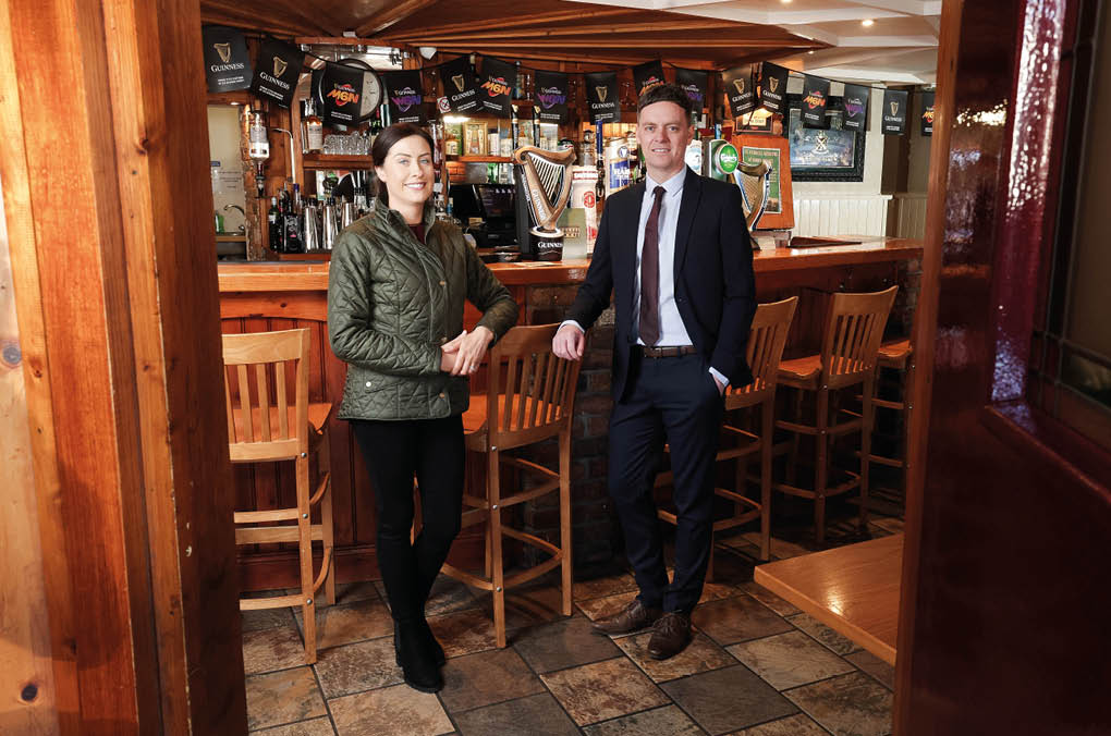 A man and woman standing in a bar. Description generated by AI