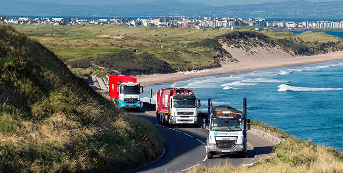 A truck is driving on a road near the ocean, with another truck following behind it. The road is curvy and overlooks the ocean, providing a scenic view for the drivers. AI generated content