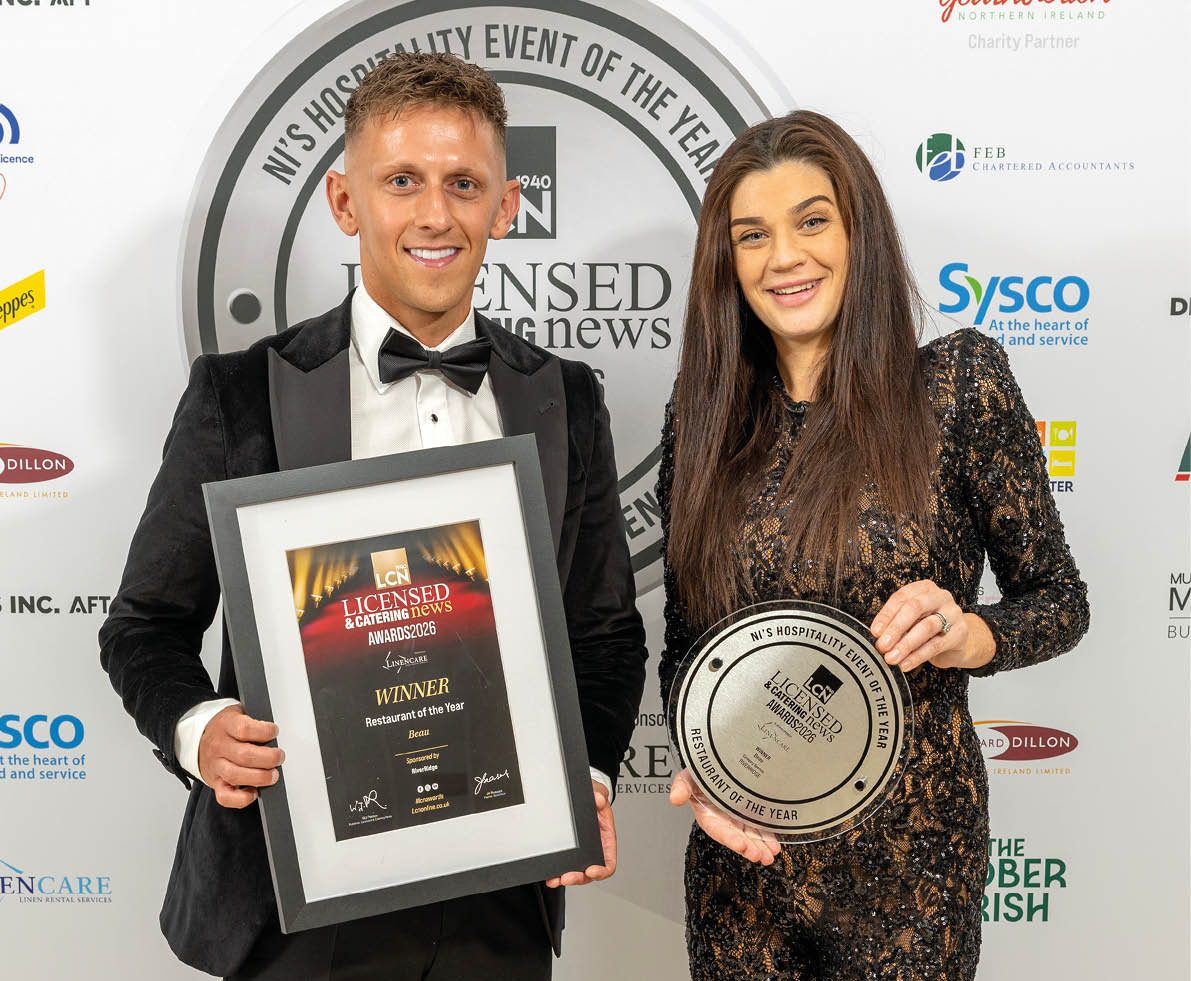 Two adults dressed in formal attire smile while holding framed awards at a hospitality event. Description generated by AI
