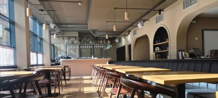 A construction site with building materials and tools in the top half and a modern, sunlit dining area with wooden tables and chairs in the bottom half. Description generated by AI