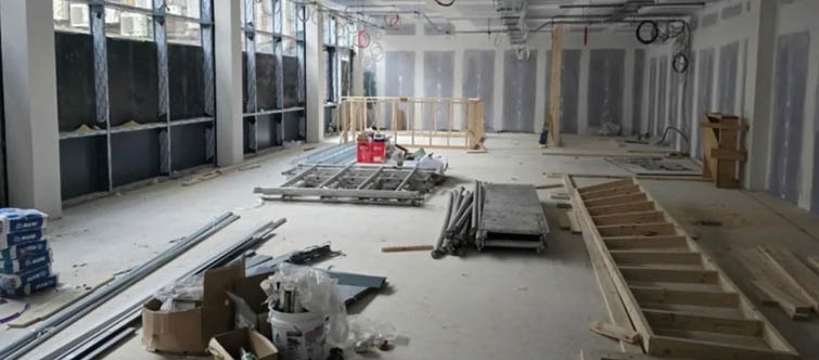 A construction site with building materials and tools in the top half and a modern, sunlit dining area with wooden tables and chairs in the bottom half. Description generated by AI