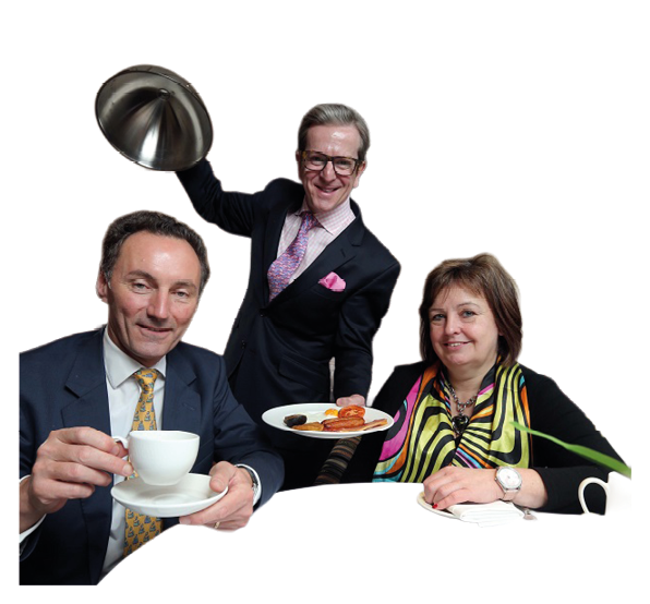 Three adults dressed in formal attire are seated at a table with one holding a cup and saucer, another holding a plate of food, and the third lifting a serving dome lid with a smile. Description generated by AI