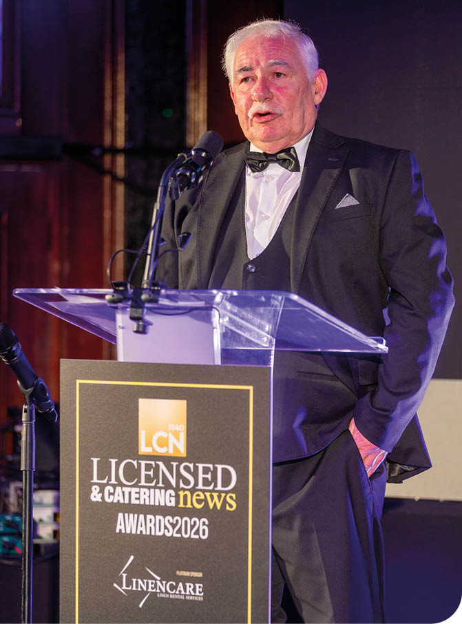 A senior person wearing a tuxedo with a bow tie is speaking at a podium with a microphone during an awards event. Description generated by AI
