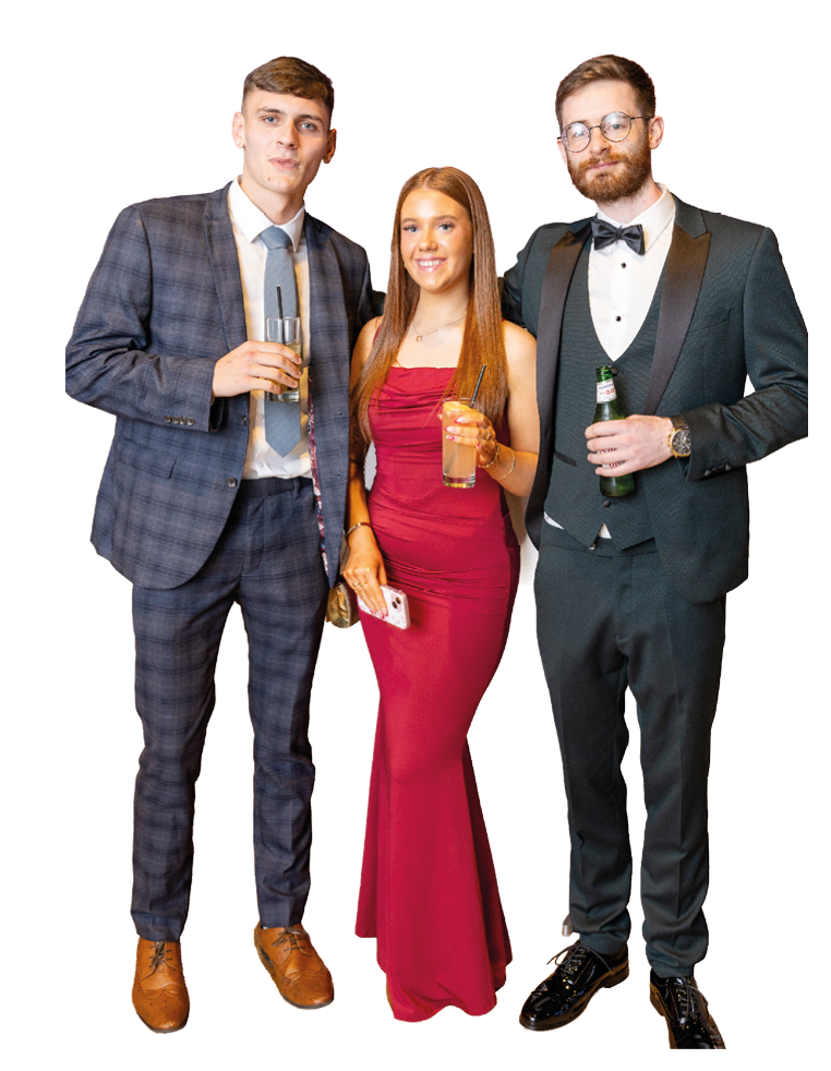 Three adults dressed in formal attire are standing together holding drinks and smiling. Description generated by AI